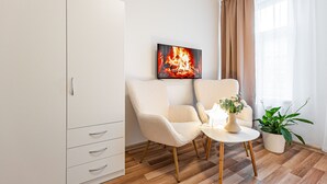A modern room with a white wardrobe, two chairs, a small table with a vase and plant, and a painting of a fire on the wall. - Karlsbad Apartments (Karlovy Vary)