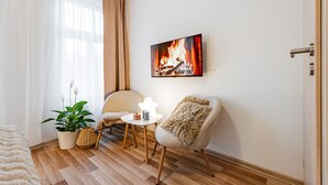 A cozy room with a fireplace, a potted plant, a small table, and a comfortable chair. - Karlsbad Apartments (Karlovy Vary)