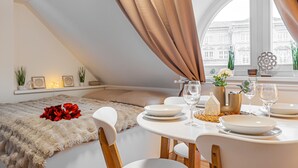 A dining area with a table set for two, a fur throw on the bed, and a view of a building through a window. - Karlsbad Apartments (Karlovy Vary)