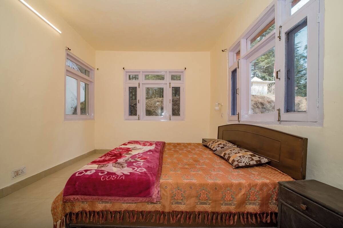 Ein Schlafzimmer mit einem Bett, einem Nachttisch und zwei Fenstern.