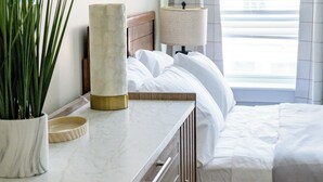 Habitación de hotel con cama, mesita de noche, lámpara, espejo y planta en maceta.