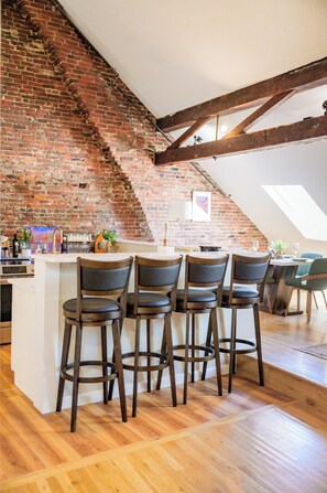 A kitchen with a brick wall, wooden beams, and a bar area with stools. - Market Square Inn (Portsmouth)