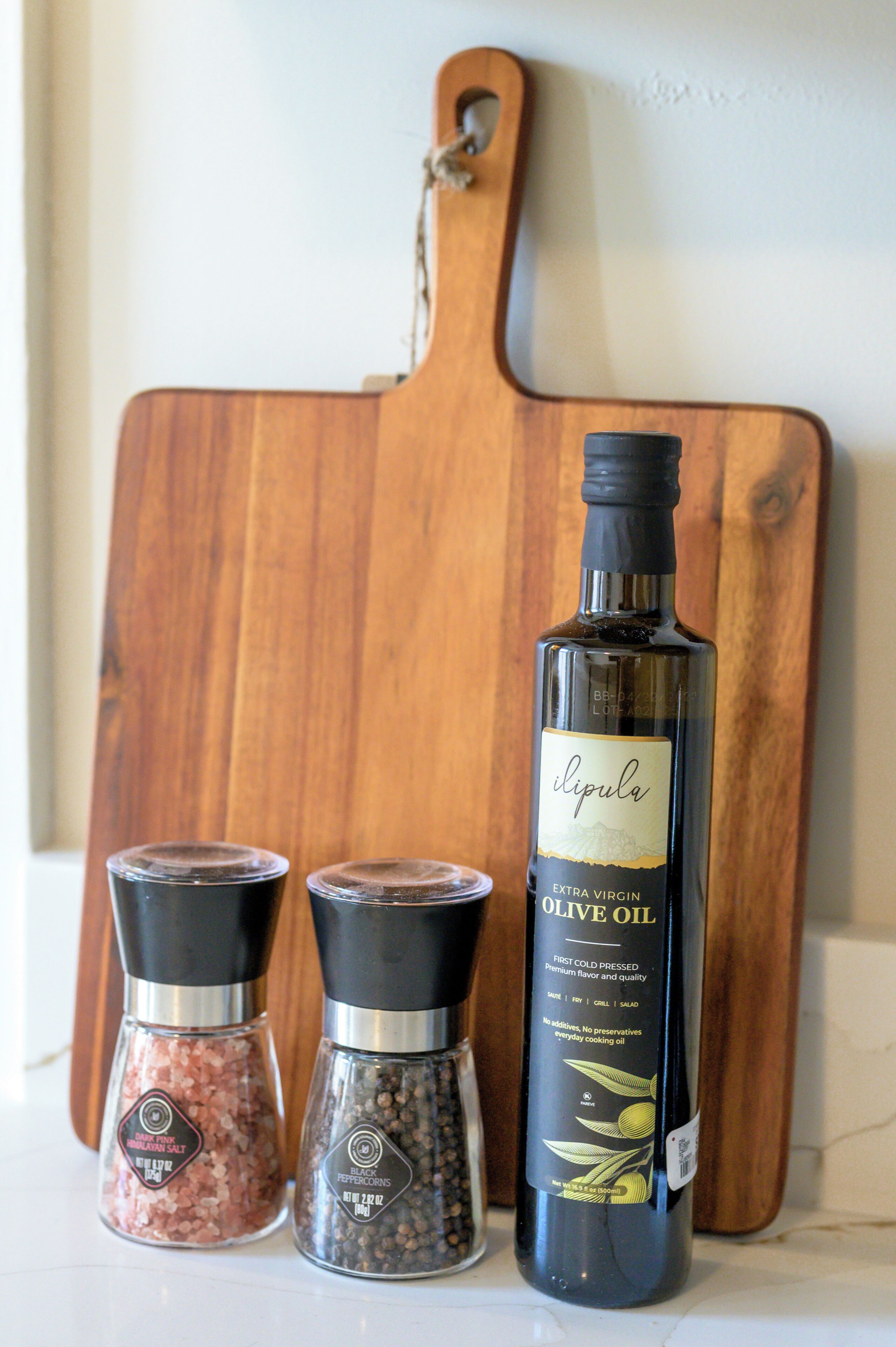 Uma garrafa de azeite extra virgem, dois recipientes de pimenta do reino e uma tábua de corte de madeira.
