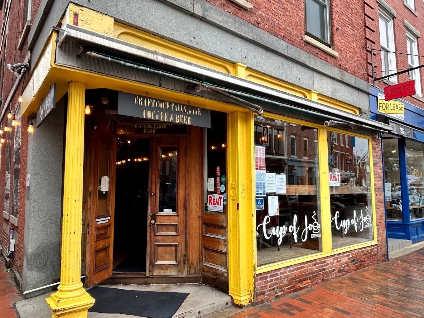 A storefront with a sign for a coffee and beer shop, a visible door, and a window with a sign that reads 'Cup of Joe Coffee & Beer'.