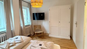 Ett sovrum med två sängar, en stol, en tv och en garderob.