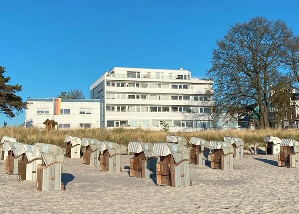 A row of beach huts numbered 37 to 69 on a sandy beach, with a large building in the background.
