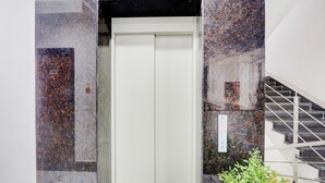 An elevator with a white door, surrounded by granite tiles with speckled patterns. - Super Townhouse Oak Garden (Hanmakonda)