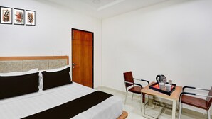 A hotel room with a bed, a wooden door, a table with chairs, and a coffee maker. - Super Townhouse Oak Garden (Hanmakonda)
