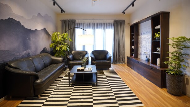 A modern living room with a black and white checkered rug, a sofa, two armchairs, a coffee table, and a bookshelf.