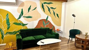 A room with a green sofa, a white coffee table, a wooden floor, and a wall with abstract leaf patterns.