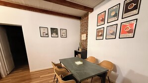 A dining area with a table and chairs, framed coffee posters on the wall, and a brick accent wall.