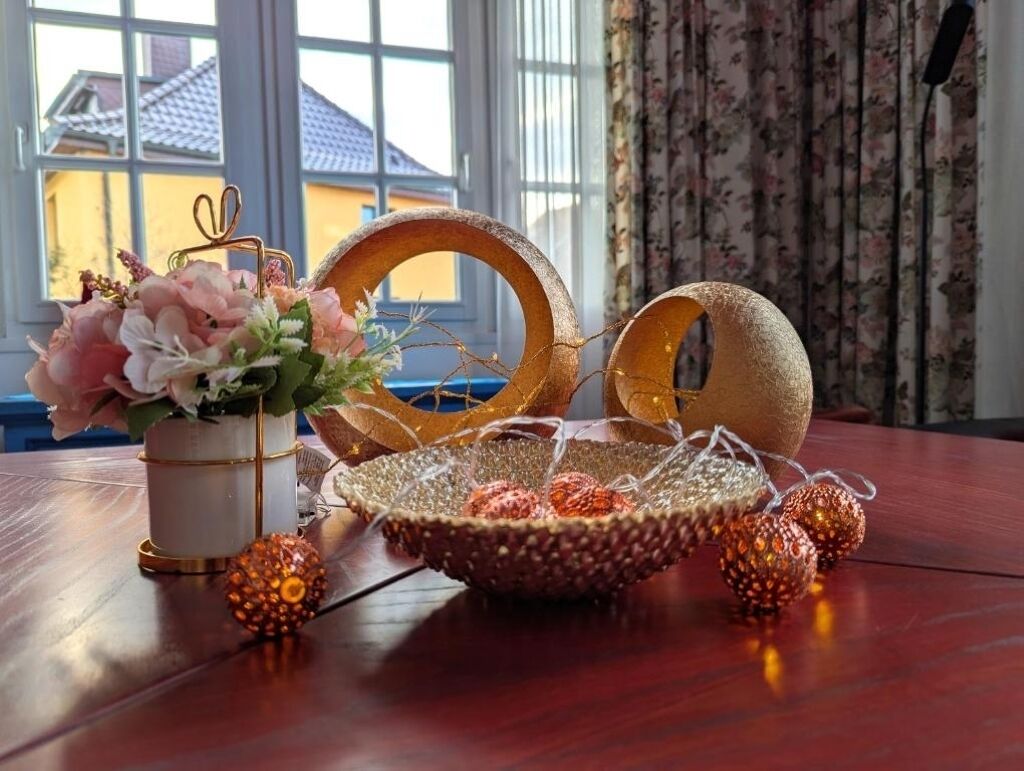 Een houten tafel met een bloemenvaas, een gevlochten mand en decoratieve verlichting.
