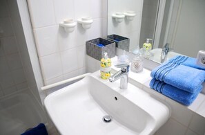 Ein Badezimmer mit einem weißen Waschbecken, einem Spiegel, einem Handtuchhalter und Toilettenartikeln.