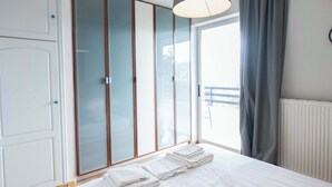 A bedroom with a bed, white curtains, a window, and a wardrobe with frosted glass doors.