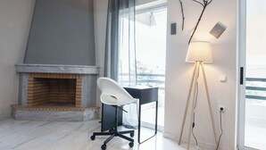 A modern room with a fireplace, a desk with a chair, a floor lamp, and a large window.