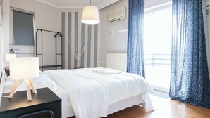 A bedroom with a bed, a desk with a lamp, a radiator, and a window with curtains.