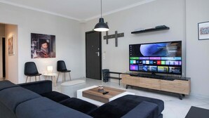 A modern living room with a flat-screen TV, black sofas, a coffee table, and a minimalist design.