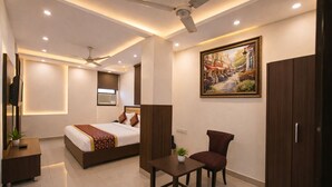 Una habitación de hotel moderna con una cama, un escritorio, una silla, un armario, un ventilador de techo, iluminación empotrada y un cuadro en la pared.