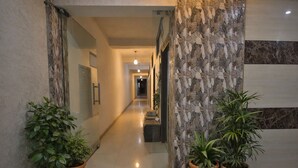 Un pasillo con pared de piedra, plantas en macetas y una puerta que da a otra habitación.