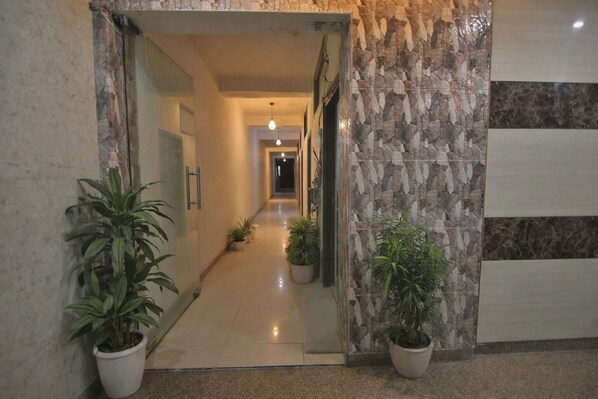 Un pasillo con paredes de piedra, plantas en macetas y una puerta que conduce a otra habitación.