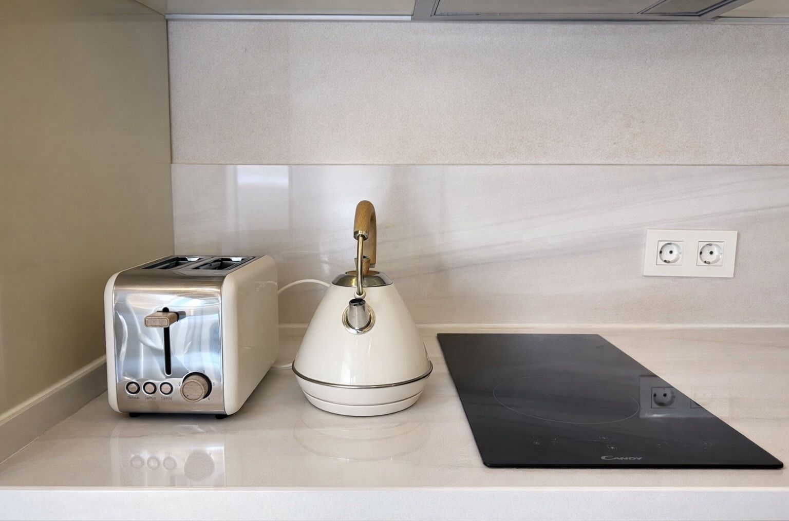 Une cuisine équipée d’un grille-pain, d’une bouilloire et d’une plaque de cuisson à induction, le tout posé sur un plan de travail.