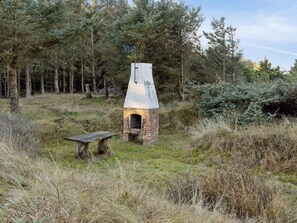 Ein rustikaler Backofen aus Ziegelsteinen im Freien mit Schornstein, umgeben von Bäumen und Gras.