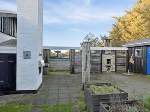 A courtyard with a brick wall, a wooden gate, a blue door, and a small brick oven. - 4 Star Holiday Home in Lokken (Lokken)