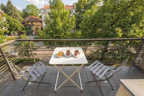Ein Balkon mit Tisch für Zwei, zwei Stühlen und Blick auf Gebäude und Bäume.
