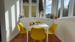 Zona pranzo con tavolo bianco e sedie gialle, una decorazione a girasole e una finestra vista casa e alberi.