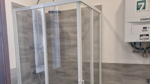 Una cabina doccia in vetro con design moderno, una parete rivestita di piastrelle e un scaldabagno.