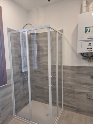 Eine gläserne Dusche mit modernem Design, eine Kachelwand und ein Warmwassergerät.
