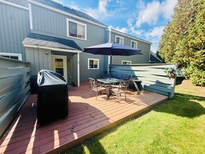 A deck with outdoor furniture, a grill, and a house in the background.