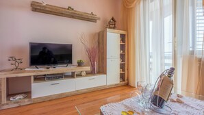 Un salon avec un téléviseur, un meuble de rangement en bois, un meuble blanc et une table en verre décorée de bougies.
