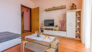 Un salon moderne avec une table basse en verre, un canapé, un téléviseur, un meuble en bois et une porte donnant sur une autre pièce.