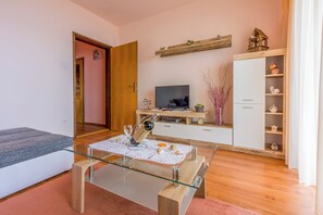 A modern living room with a glass coffee table, a sofa, a TV, a wooden cabinet, and a door leading to another room. - Apartment with balcony, sea view and fitness room (Crikvenica)