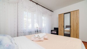 Une chambre à coucher avec un lit, une armoire en bois et une fenêtre ornée de rideaux légers.