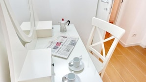 Ein weißer Tisch mit einer Zeitung, einer Kaffeekanne, zwei Tassen und einem Stuhl.