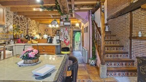 A rustic kitchen with wooden beams, a stone wall, and a staircase with patterned tiles.