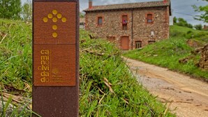A signpost with a logo and text, a dirt path, and a stone building in the background.