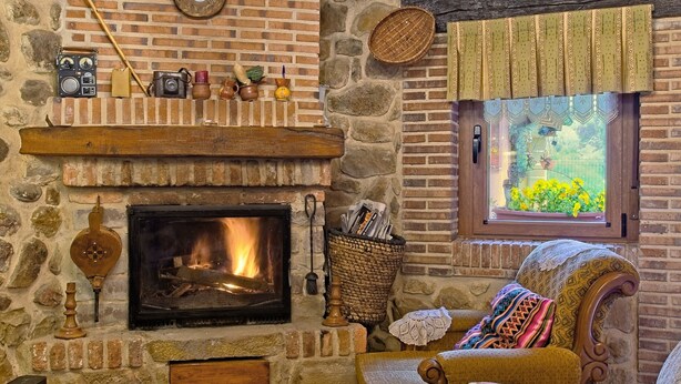 A stone fireplace with a fire, a wooden mantel, and a rustic chair.