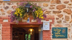 A stone building entrance with a flower arrangement, a number sign, and a green sign with text.