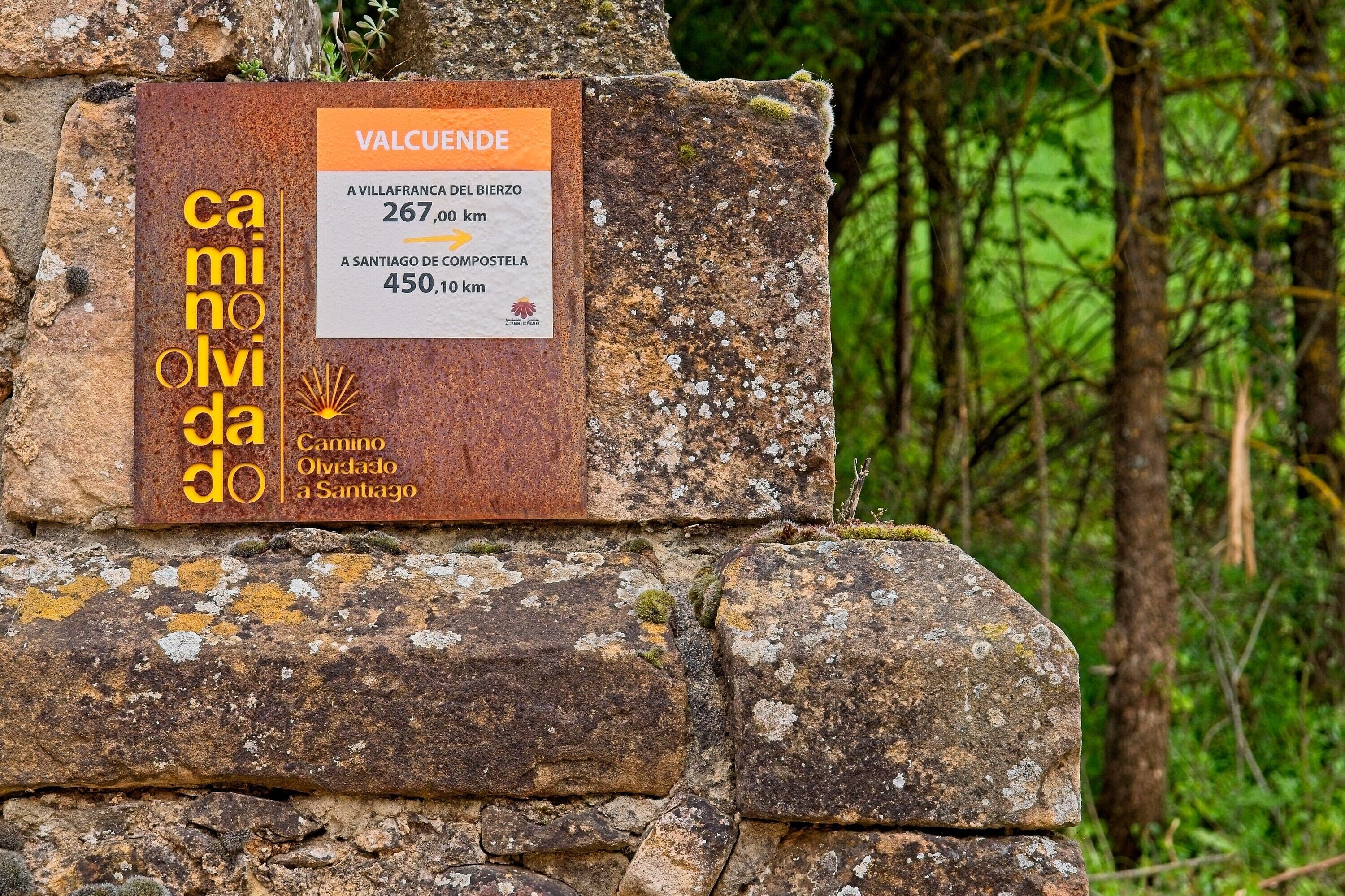 Uma placa de pedra com texto e um logotipo, ao fundo uma paisagem natural.