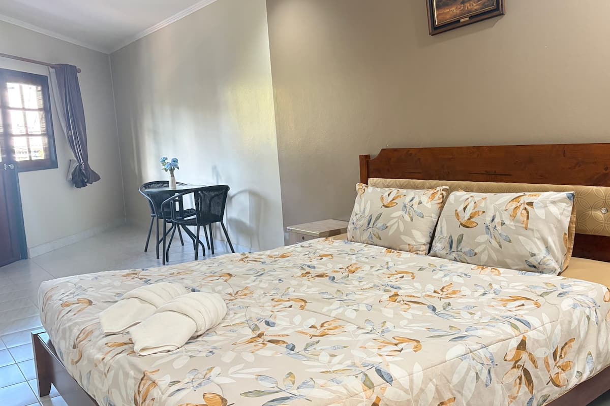 Una cama bien tendida con ropa de cama floral, un cabecero de madera y una pequeña mesa con una silla a un lado.