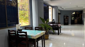 Un comedor con mesas y sillas, una planta en maceta y una estantería.