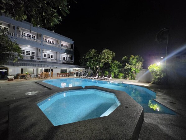 A swimming pool with lounge chairs, a dining area, and a building with multiple floors and balconies. - Collection O Southern Star Resort (Pattaya)