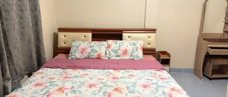 A bed with floral bedding, a wooden headboard, and a nightstand with a mirror.