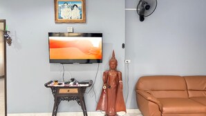 Una sala de estar con televisor, una estatua, un ventilador y un sofá.