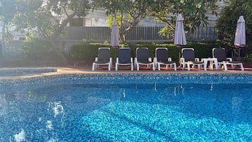 Ein Swimmingpool mit gefliesten Rändern, umgeben von weißen Liegestühlen und Sonnenschirmen.