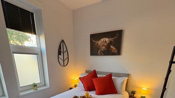 A neatly made bed with a green blanket, red pillows, and a small bedside table with a lamp. - Contemporary City Studio 1 - Contractor's and traveller's accommodation (Peterborough)