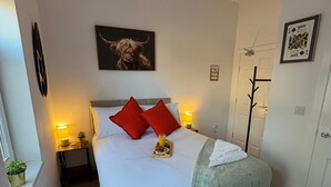 A neatly made bed with red pillows, a bedside table with a lamp, a framed picture on the wall, and a window with a plant. - Contemporary City Studio 1 - Contractor's and traveller's accommodation (Peterborough)